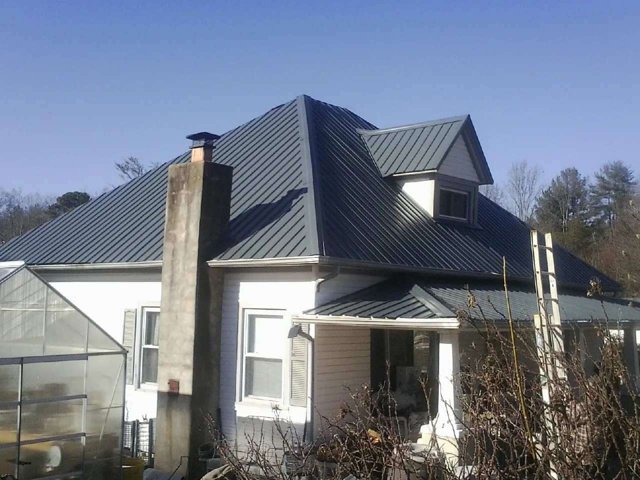 Dark blue standing seam metal roof on a white farmhouse with dormer — Slate & Tile Roof Repair by Roofing Brothers in Raynham