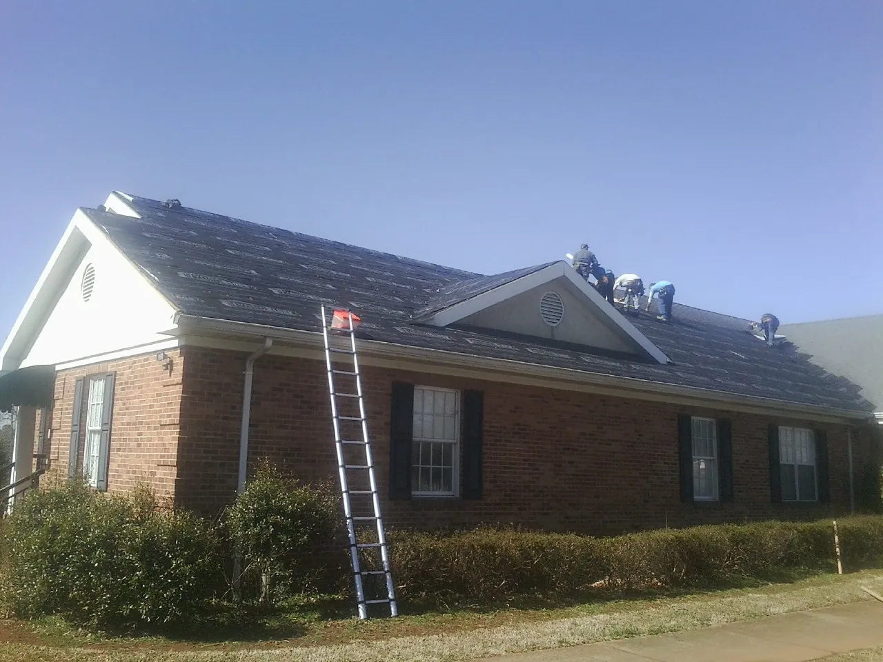 Crew tearing shingles off a brick ranch roof with a ladder set — Emergency Roof Repair work by our crew in Raynham