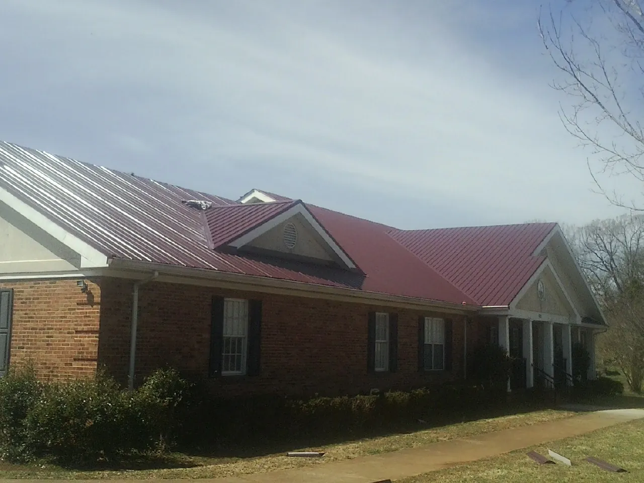 Red metal roof with gabled entries on a long brick building, from a Hail Damage Roof Repair job in Raynham