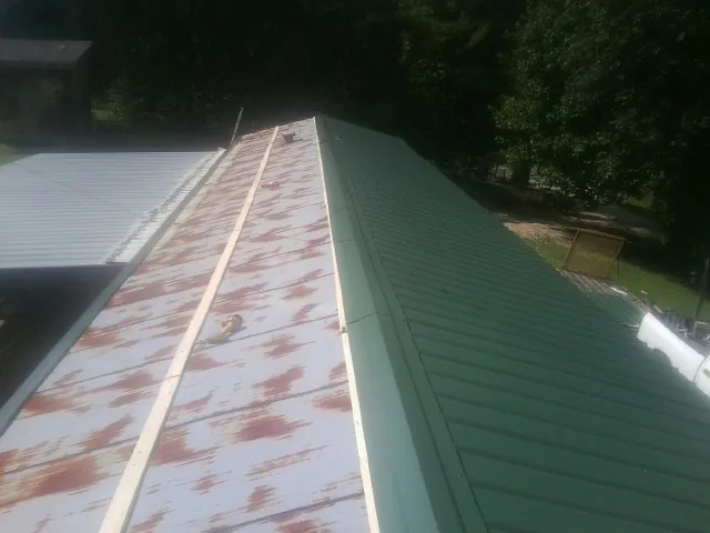 Old rusted panels beside newly installed green metal roofing — Wind Damage Roof Repair by Roofing Brothers in Raynham