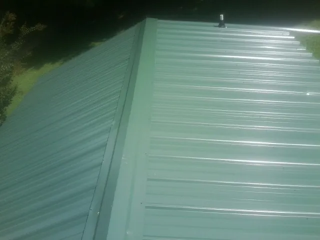 New green metal panels meeting at the ridge of a roof — Flat Roof Repair work by our crew in Raynham