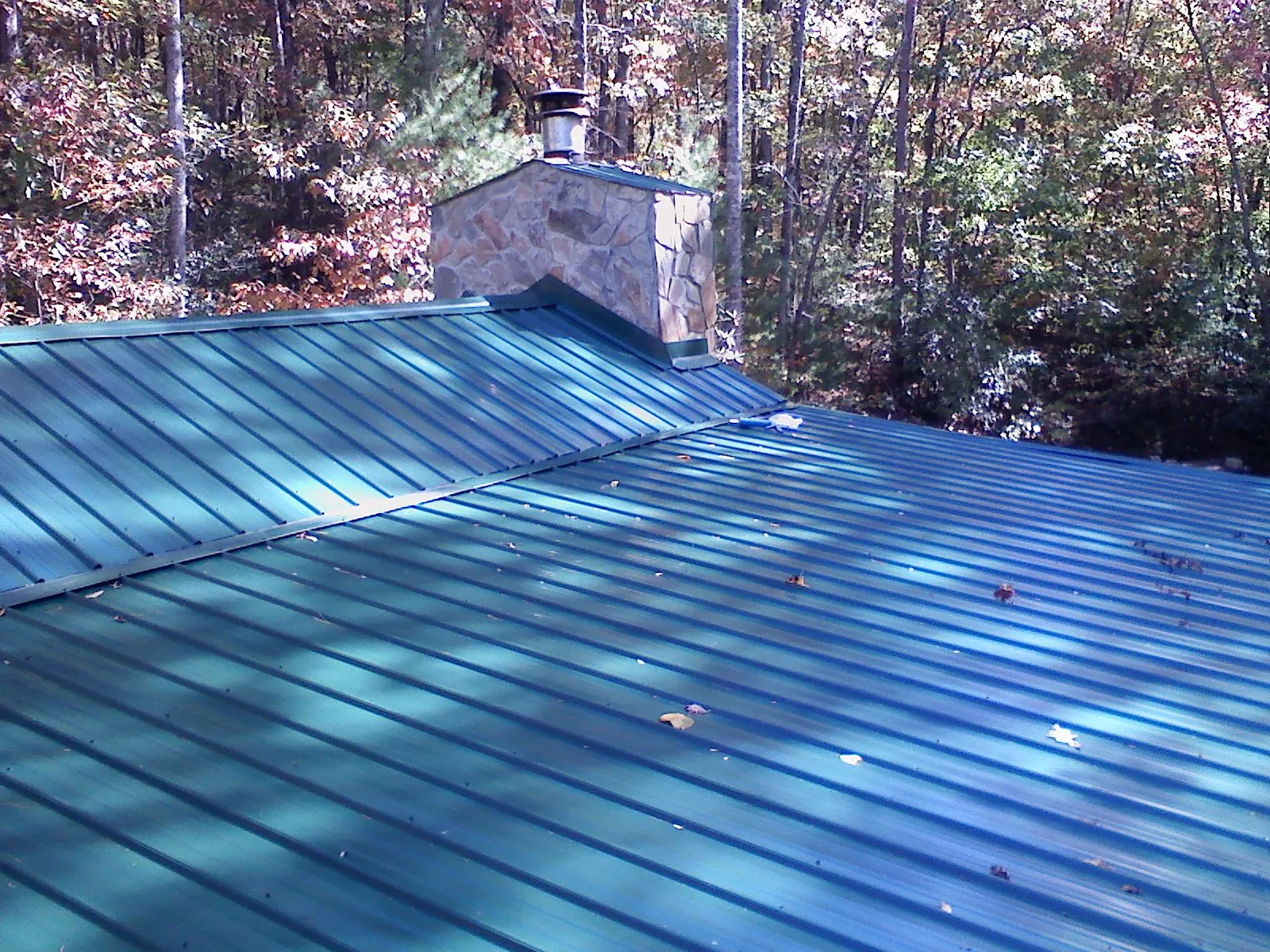 New green metal roof and stone chimney surrounded by autumn woods in Raynham