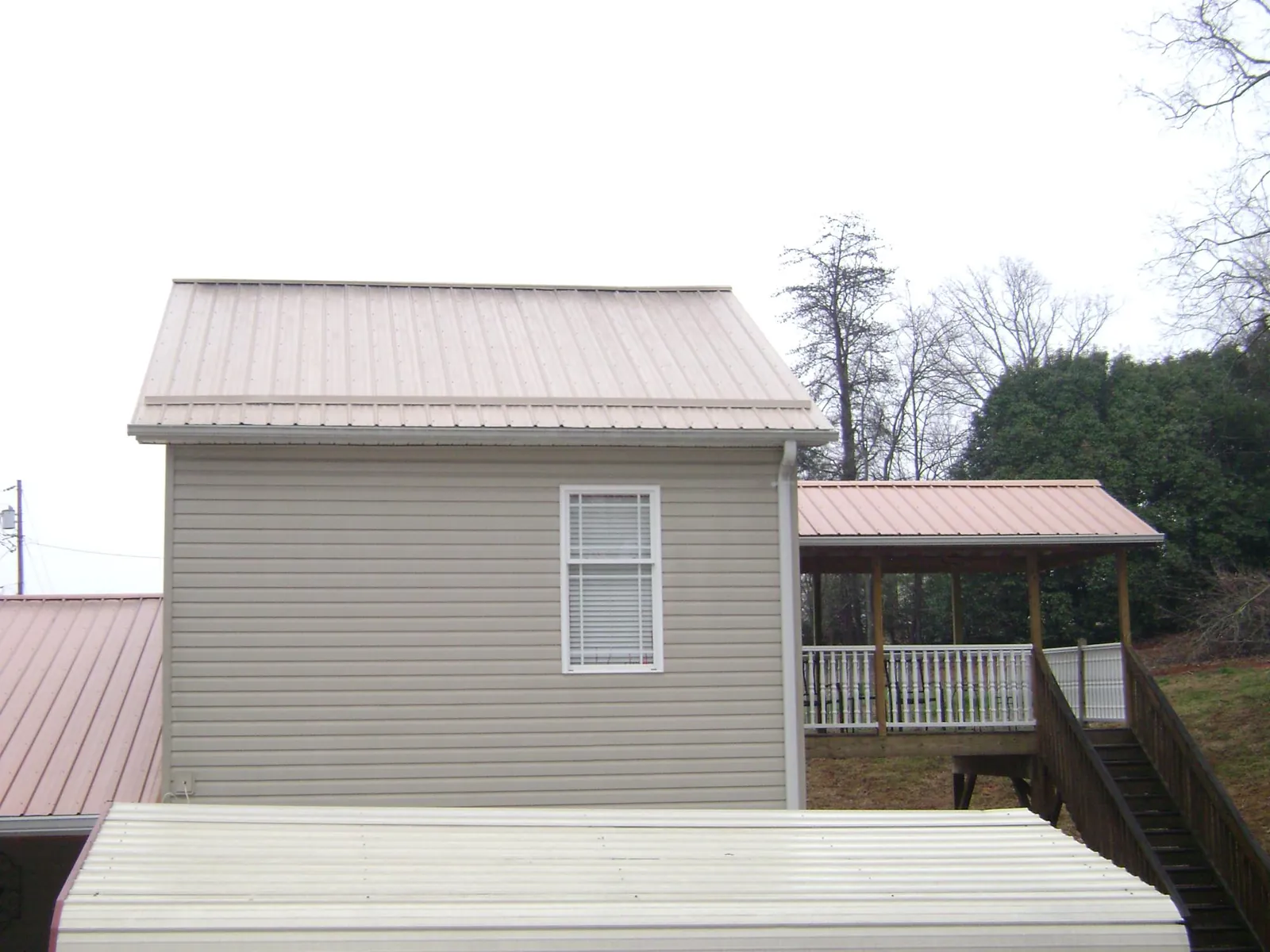 Tan metal roofs on a two story addition and attached porch, from a Roof Replacement job in Raynham
